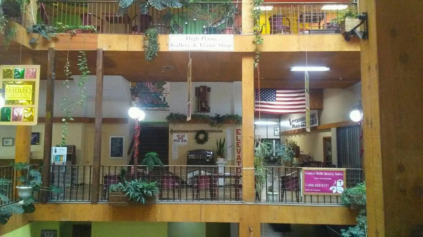Shopfronts, globe lamps, and plants along an interior balcony at The Atrium